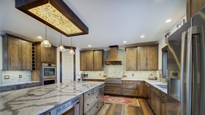 Cocina moderna con armarios de madera, una isla grande, electrodomésticos de acero inoxidable, iluminación colgante y un salpicadero con diseño.