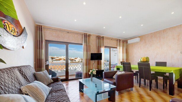 A modern living room with a sofa, a glass coffee table, a flat-screen TV, and a dining area with a table and chairs. - Apartment 'Lagos Terrace Villa' with Private Terrace, Wi-Fi and Air Conditioning (Lagos)