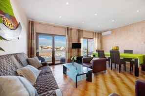 A modern living room with a sofa, a glass coffee table, a flat-screen TV, and a dining area with a table and chairs. - Apartment 'Lagos Terrace Villa' with Private Terrace, Wi-Fi and Air Conditioning (Lagos)