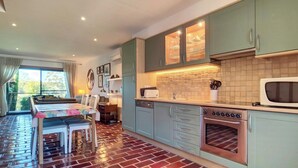 A kitchen with a dining area, a brick-patterned floor, and a view of greenery outside.
