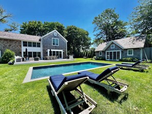 Ein Garten mit Swimmingpool, zwei Liegestühlen und einer Terrasse mit Gartenmöbeln.