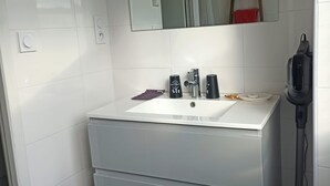 Une salle de bain avec un lavabo blanc, un miroir et un aspirateur.
