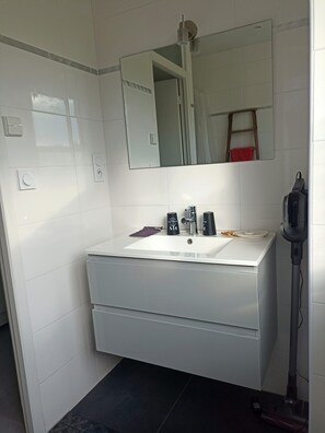 Een badkamer met een witte wastafel, spiegel en stofzuiger.