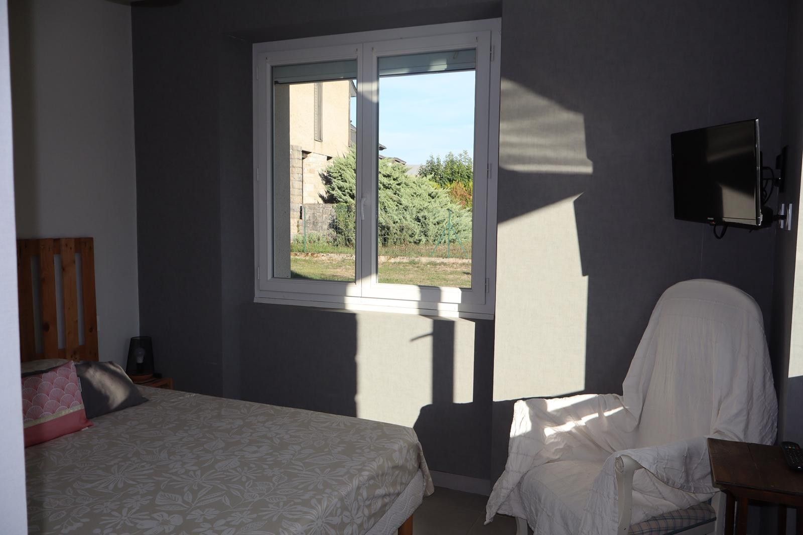 Ein Schlafzimmer mit Bett, Sessel, Fernseher und Fenster mit Blick auf Grünflächen.