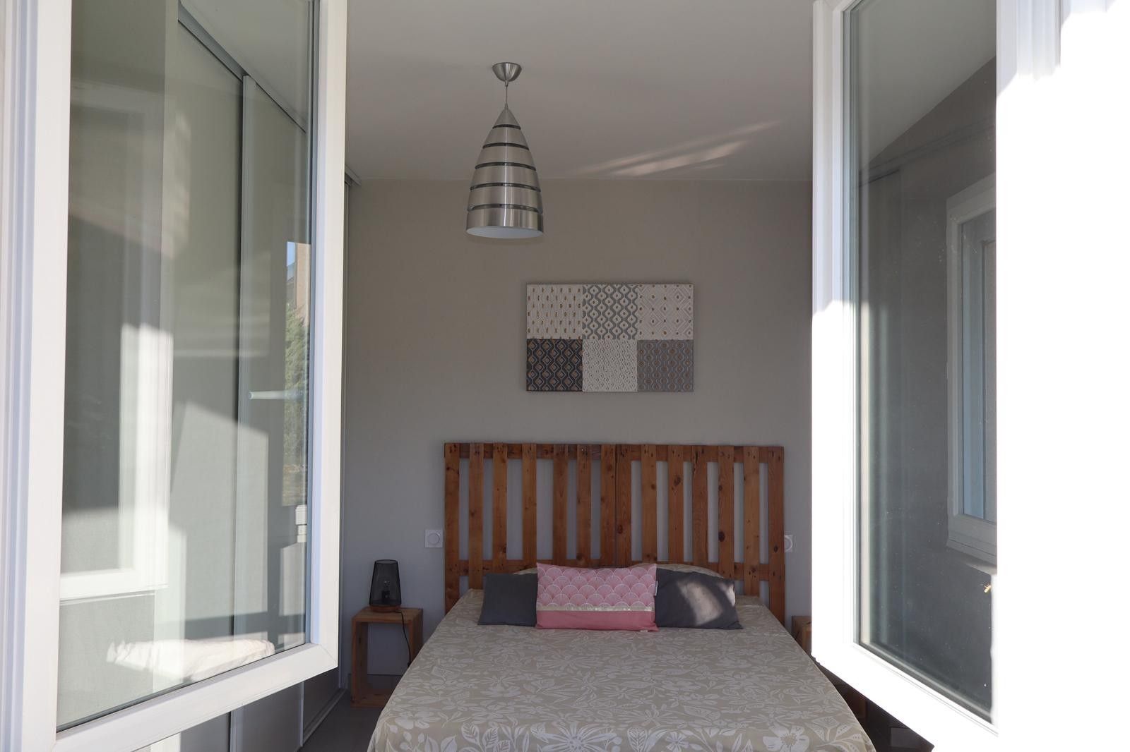 A bedroom with a bed, a headboard, a bedside table, a lamp, and a wall-mounted light fixture.