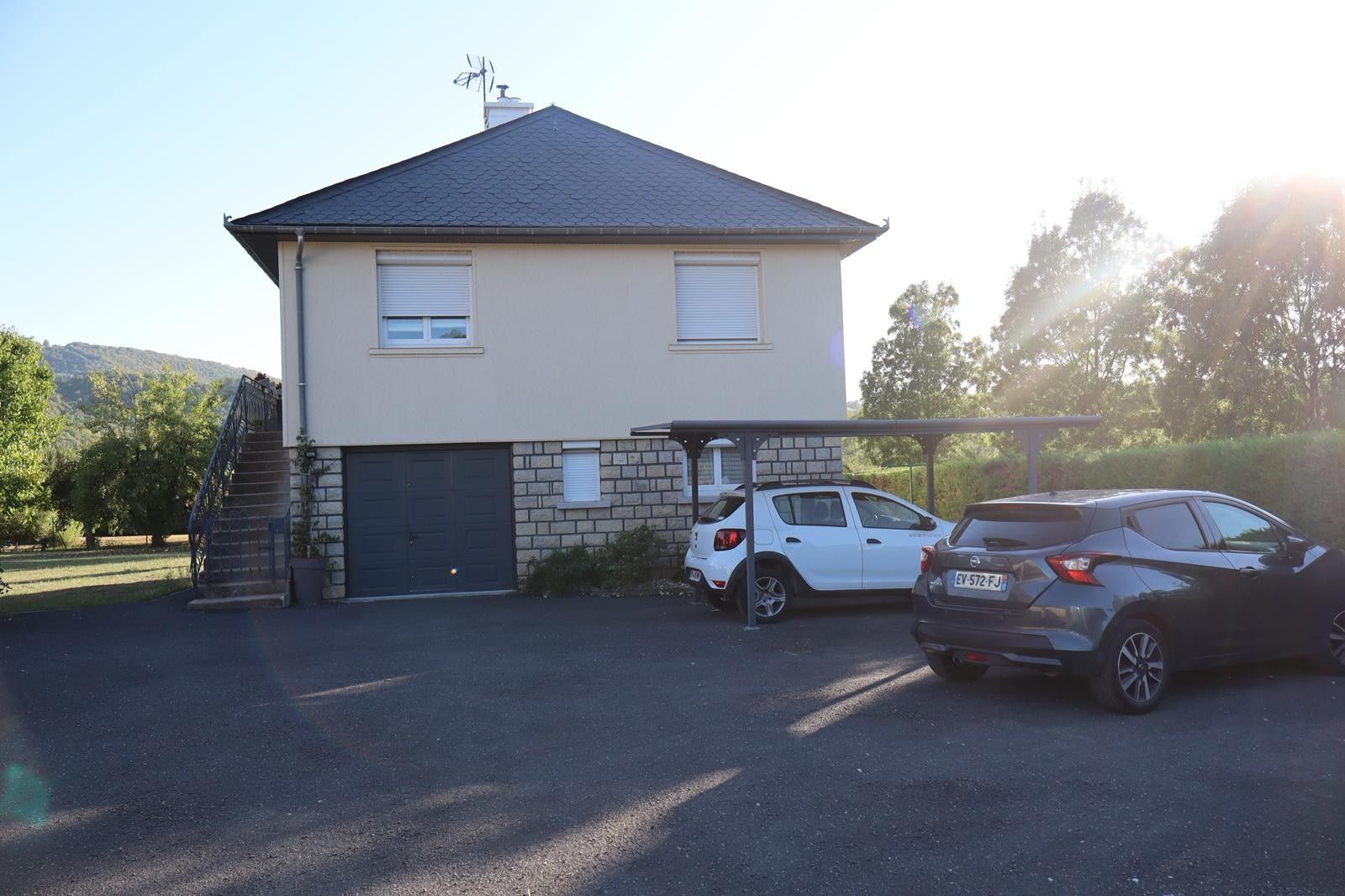 Une maison à deux étages avec un garage, deux voitures garées et un escalier menant à l’entrée.
