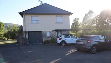 Une maison à deux étages avec un garage, deux voitures garées et un escalier menant à l’entrée.