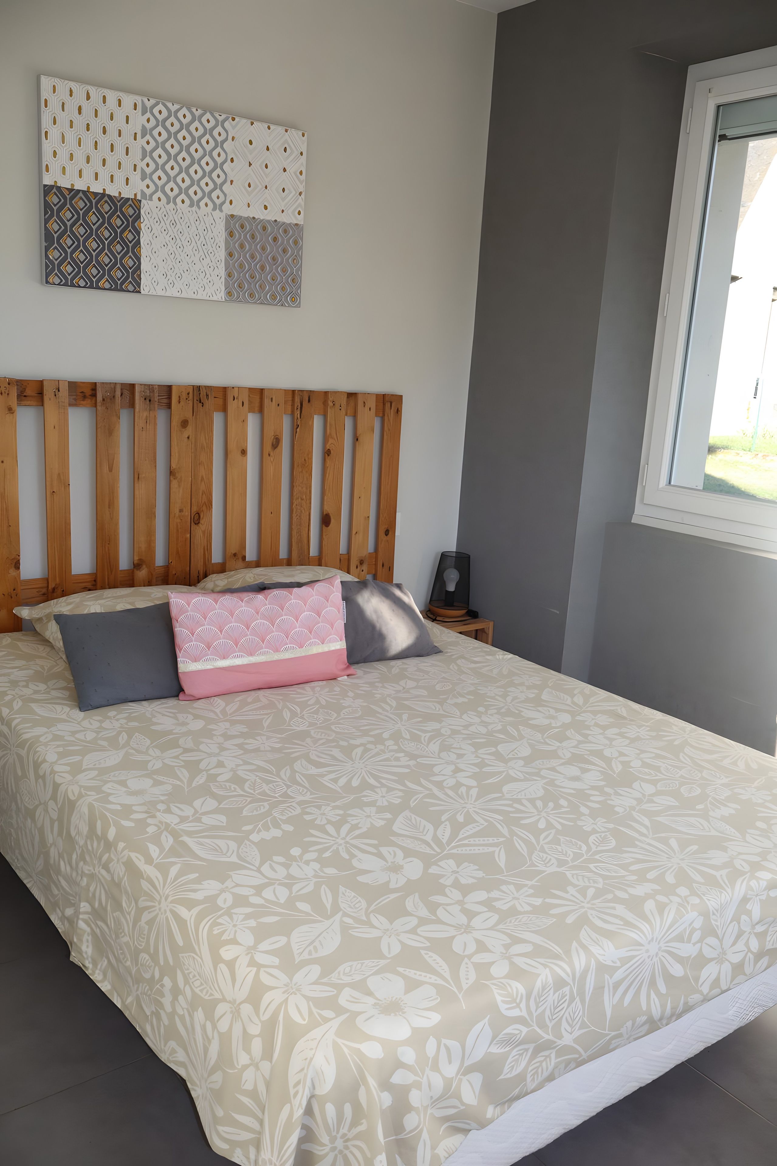 A bedroom with a wooden headboard, a floral-patterned bedspread, and a wall-mounted decorative panel.