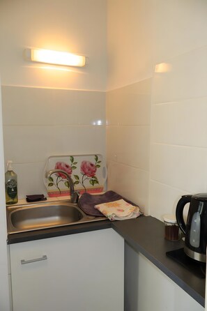 Een kleine keuken met een spoelbak, een waterkoker en een fles handzeep.