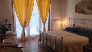 A bedroom with a bed, curtains, a bedside lamp, a dresser, and a mirror.