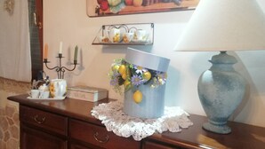 A wooden dresser with a lace doily, a blue vase with flowers, a tea box, and a lamp.