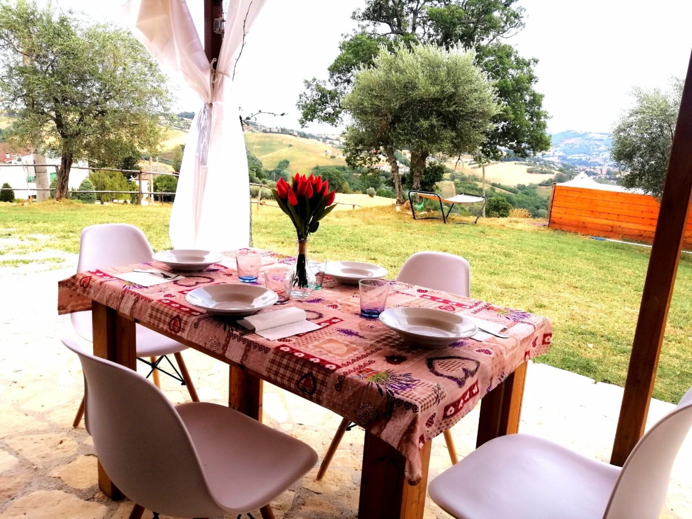 Een buitenterras met een tafel voor vier personen, omringd door stoelen, en uitzicht op een glooiend landschap.
