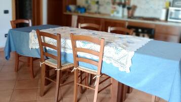 Ein Essbereich mit Tisch, der mit einer blauen Tischdecke bedeckt ist, Holzstühle und einer Küche im Hintergrund.