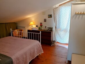 A bedroom with a bed, a dresser, a lamp, and a window with a curtain.