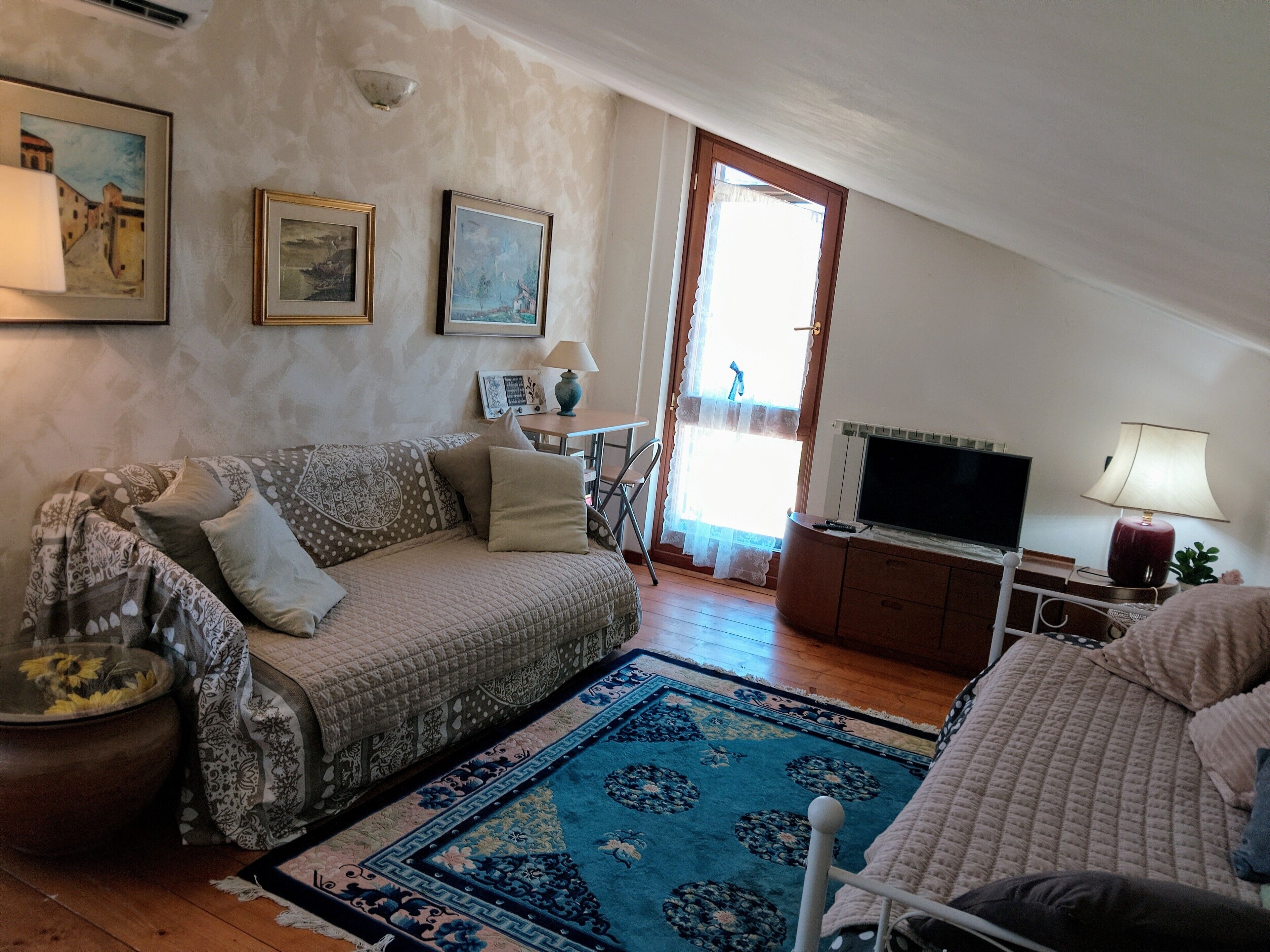 A living room with a sofa, a television, a lamp, a patterned rug, and a painting on the wall.