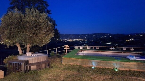 A nighttime outdoor area with a tree, a hot tub, and a grassy platform with seating.