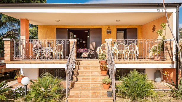 A two-story house with a covered porch, outdoor seating, and potted plants.
