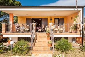 Ein zweistöckiges Haus mit überdachter Veranda, Sitzgelegenheiten im Freien und Blumentöpfen.