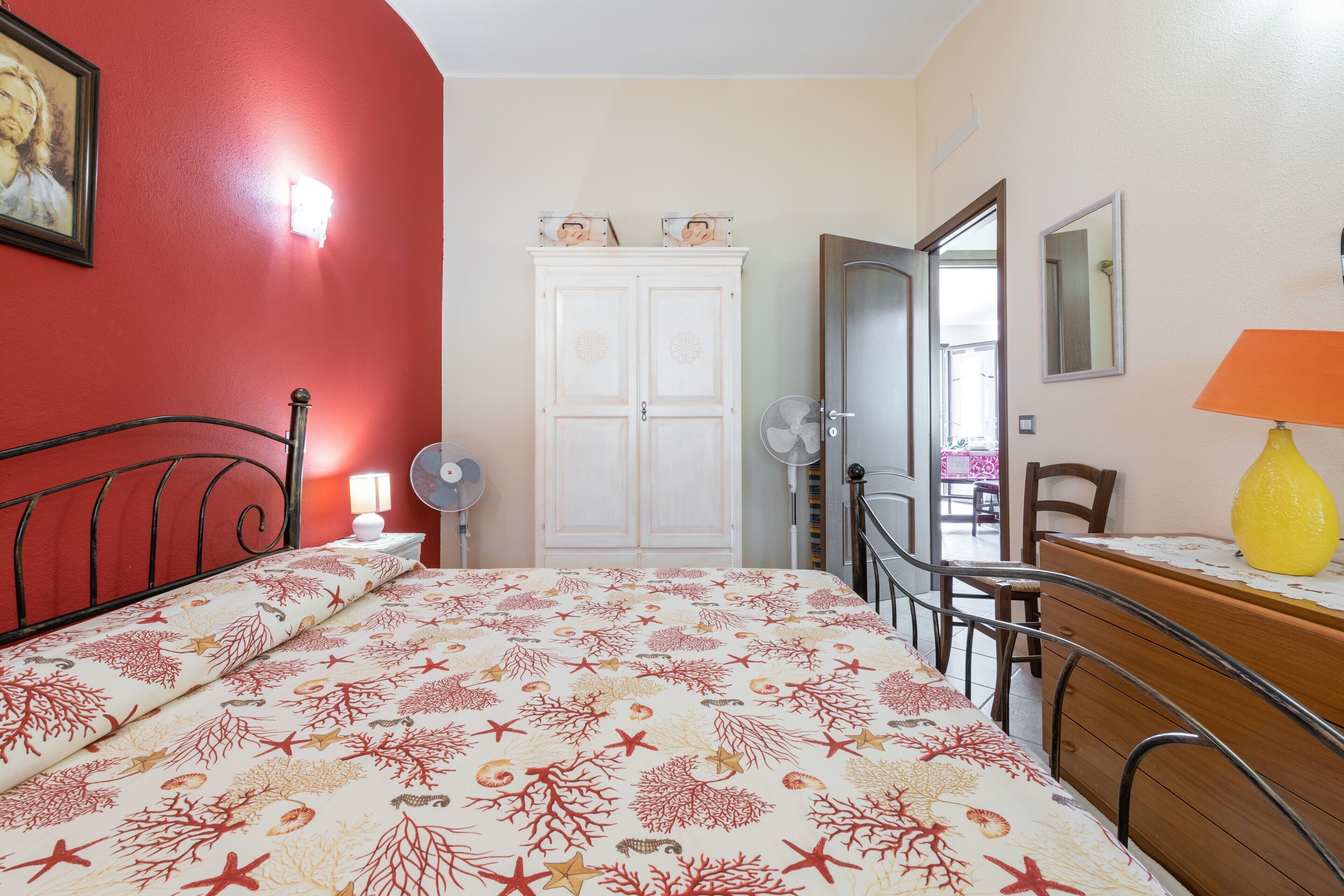 Un dormitorio con cama, cómoda, espejo, ventilador y una puerta que da a otra habitación.