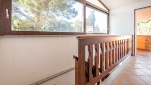 A wooden staircase with a railing, a large window with a view of trees, and a tiled floor.