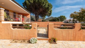 Una casa con un camino de piedra que conduce a una entrada con portón, un gran árbol y una montaña al fondo.