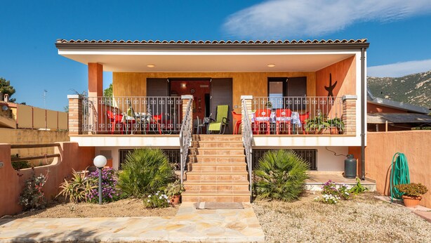 Una casa de dos pisos con un balcón, una escalera y un jardín.
