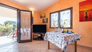 Una habitación con una mesa dispuesta para comer, un televisor y un balcón con sillas.