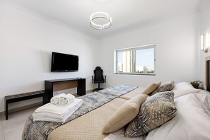 Une chambre d’hôtel moderne équipée d’un lit, d’un bureau, d’une chaise, d’une télévision et d’une fenêtre donnant sur la ville.