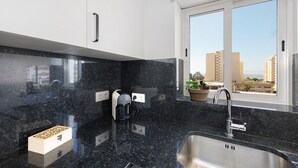 A modern kitchen with a granite countertop, a built-in coffee maker, a stainless steel sink, and a window with a city view. - Holiday Apartment 'Mar E Sol' with Balcony & Wi-Fi (Portimão)