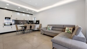 A modern kitchen with white cabinets, a dining area with chairs, and a grey sofa with a decorative pillow. - Holiday Apartment 'Mar E Sol' with Balcony & Wi-Fi (Portimão)