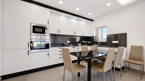 A modern kitchen with white cabinets, a built-in oven, and a dining area with a glass table and chairs. - Holiday Apartment 'Mar E Sol' with Balcony & Wi-Fi (Portimão)