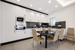 A modern kitchen with white cabinets, a built-in oven, and a dining area with a glass table and chairs.