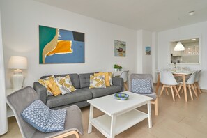 A modern living room with a grey sofa, a white coffee table, and a dining area with a white table and chairs.