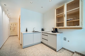 A compact kitchen with white cabinets, a countertop, a built-in oven, and a wooden cabinet above the sink.
