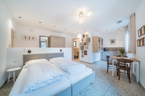 A hotel room with a bed, a small table, a chair, a kitchenette, and a bathroom.