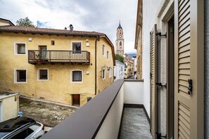 A narrow alleyway with a yellow building, a balcony, and a clock tower in the distance.