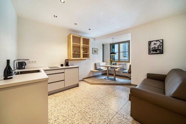 A compact kitchen with a coffee maker, a wooden cabinet, and a dining area with a table and chairs.