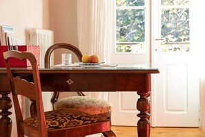 A wooden dining table with a chair, a glass, and a plate with fruit.