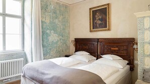 Una cama doble con cabecera de madera, un radiador, una ventana con cortinas y un cuadro enmarcado en la pared.