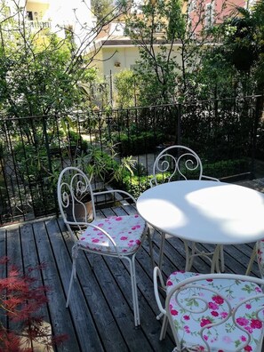 A patio with a white metal table and chairs, surrounded by greenery and a metal fence.