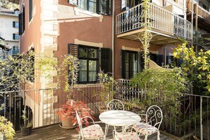 A balcony with a table and chairs, surrounded by potted plants and a metal railing.
