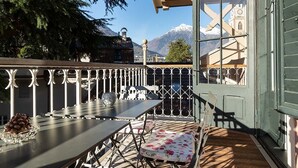 Un balcon avec une table et des chaises, une vue sur les montagnes et un bâtiment doté d’un clocher.