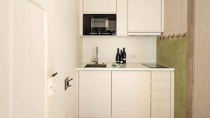 Cocina compacta con armarios blancos, un microondas, un fregadero y una pequeña zona de encimera.
