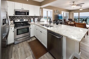 A modern kitchen with stainless steel appliances, a large island with a sink, and a view of the ocean through the balcony.