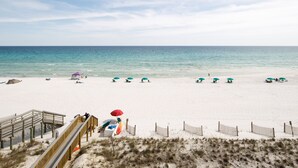 Ein Strand mit einer Holzpromenade, die zu einem Strandbereich mit Sonnenschirmen und Liegestühlen führt.