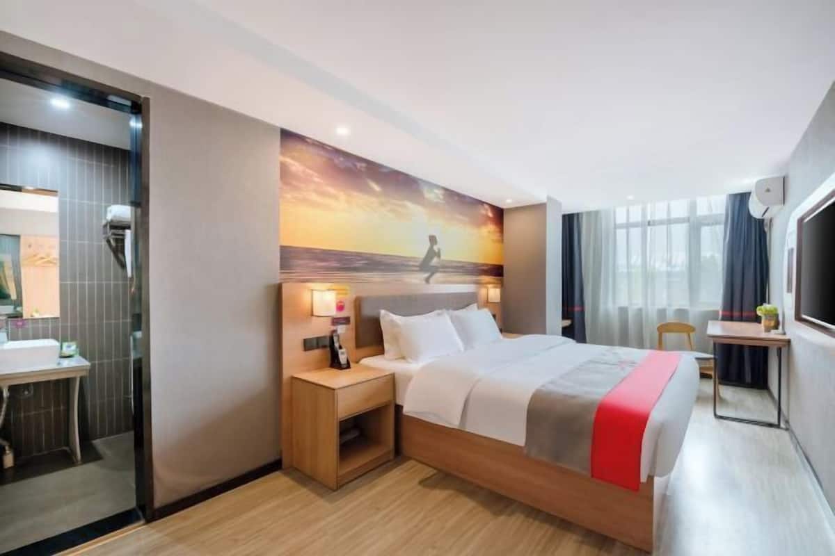 A hotel room with a bed, bedside table, nightstand, and a large window.