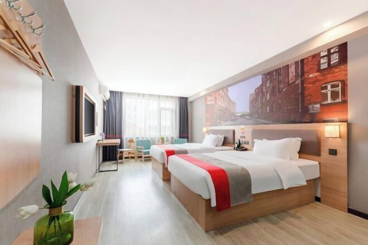A hotel room with two beds, a desk, a chair, a large window, and a wall mural.