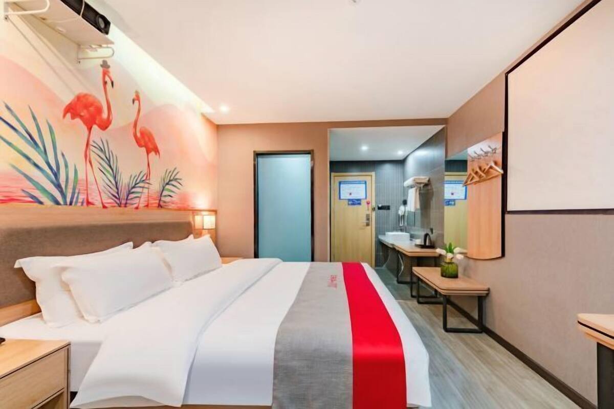 A hotel room with a bed, a desk, a chair, a mirror, and a door leading to a bathroom.
