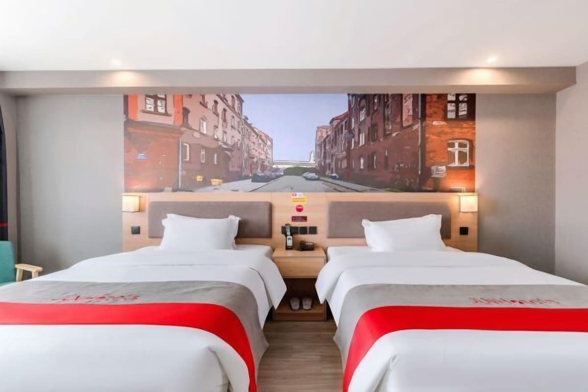 A hotel room with two beds, a cityscape mural on the wall, and a wooden floor.