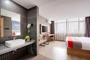 A modern hotel room with a large bed, a desk, a television, and a bathroom with a sink and mirror. - Junyi Hotel (Huaibin Mobile Building Store) (Huaibin)
